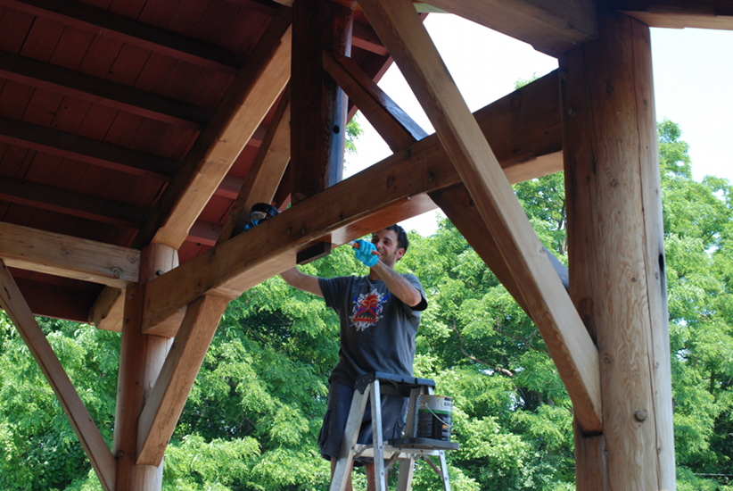 Andy, a New Energy Works timber framer works to clean one of the timber bents on the front of our Farmington New York headquarters.
