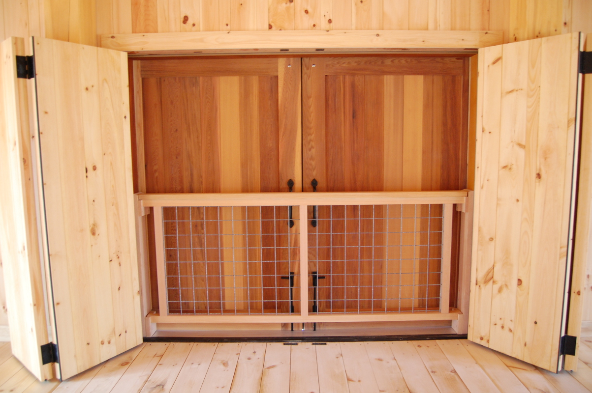 The upper level of a barn features a layered door system with folding pine doors opening to flat track hanging cedar doors.