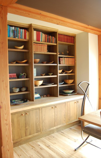 A live edge wood top with inset slab doors below and open shelves against a dark backdrop above acts as buffet, breakfront, and display space.