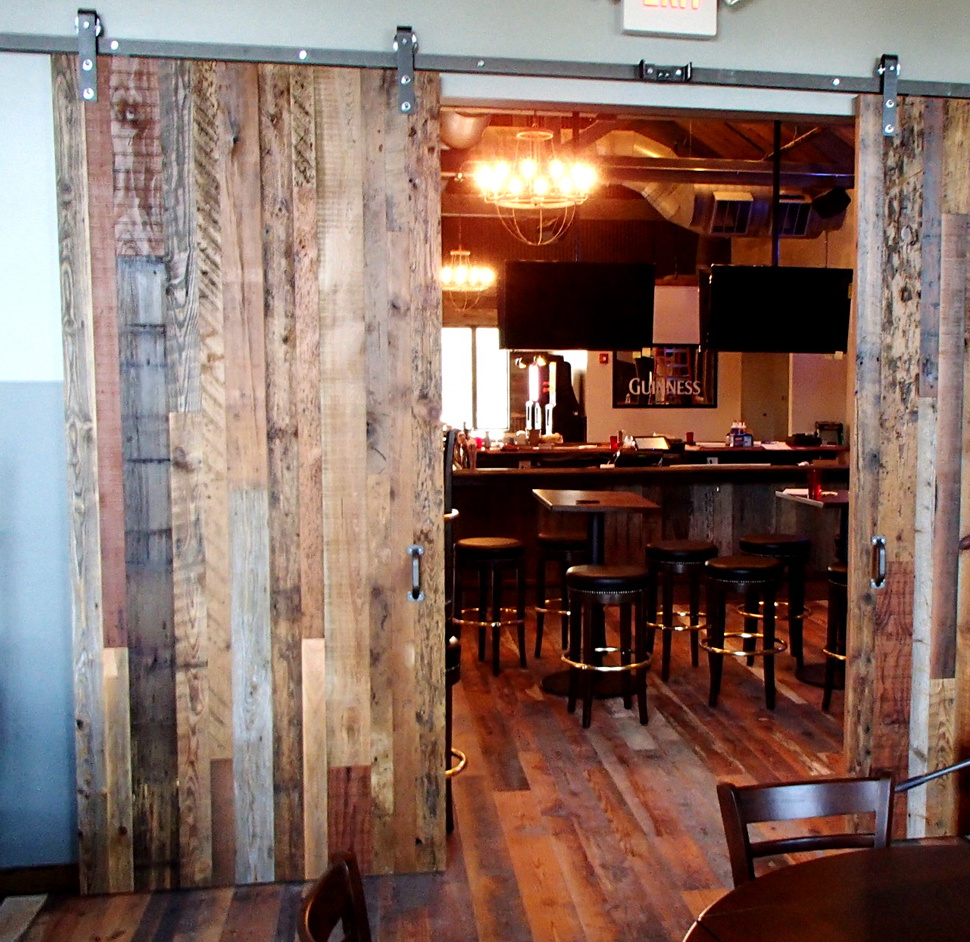 Industrial salvaged mixed woods and silvered hardware give an industrial vibe to these doors. Sliding along a track allows more space for seating and lessens the likelihood of servers or patrons unexpectedly meeting a door swinging open/closed.